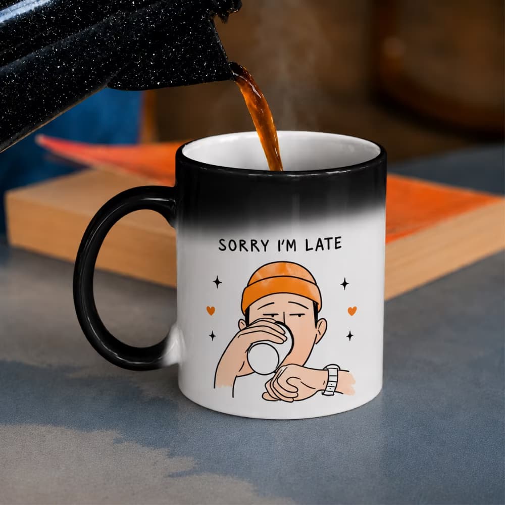 A color-changing magic mug revealing a white section with a cartoon of a man drinking coffee and the text "SORRY I'M LATE".