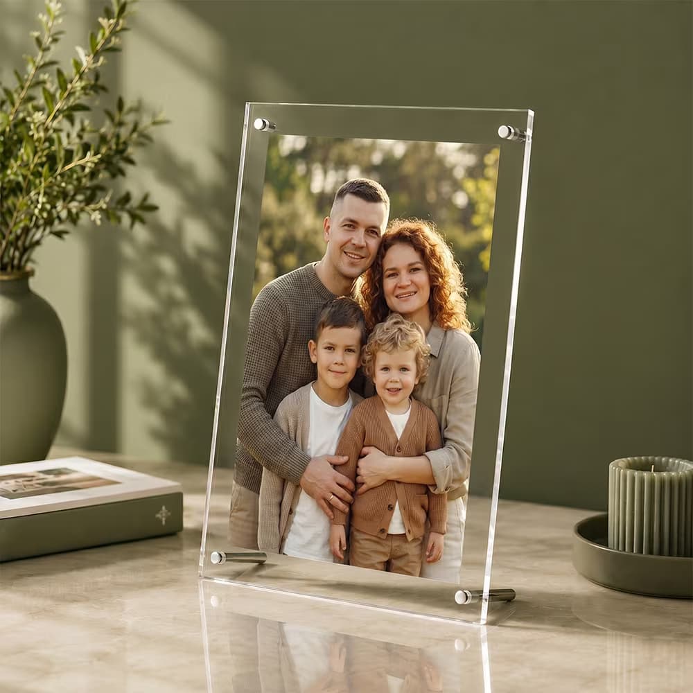 A vertical clear acrylic photo frame standing on a marble surface, displaying a portrait of a smiling family of four.
