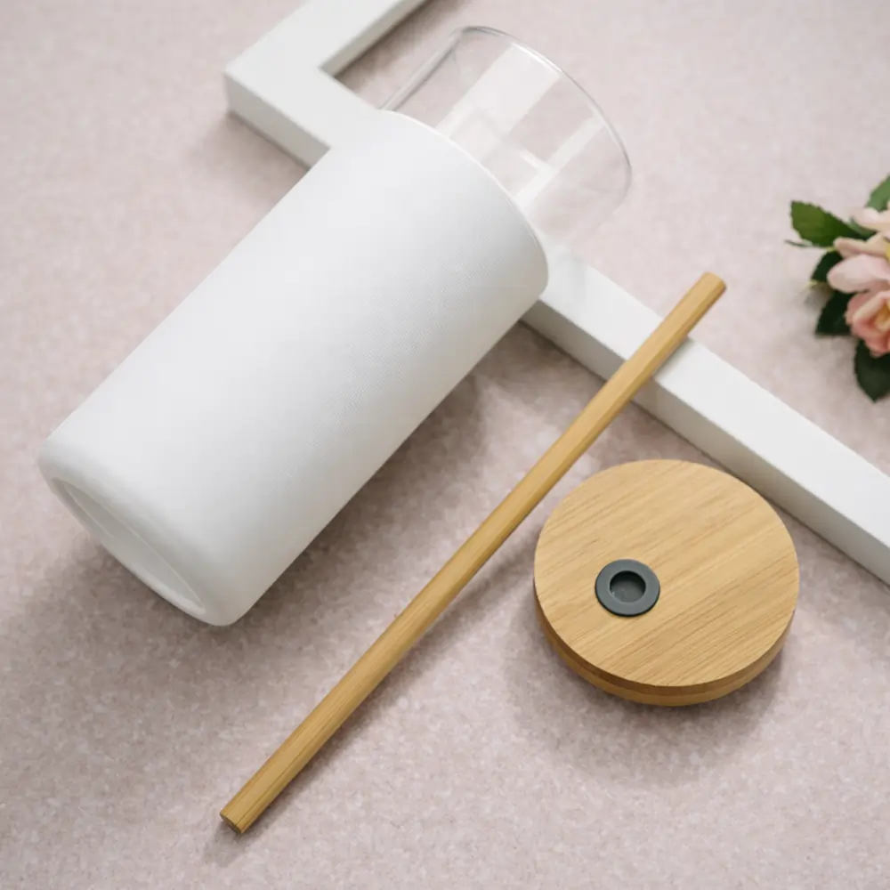 A top down view of a disassembled white glass tumbler, showing the glass body, a bamboo lid and a matching bamboo straw.