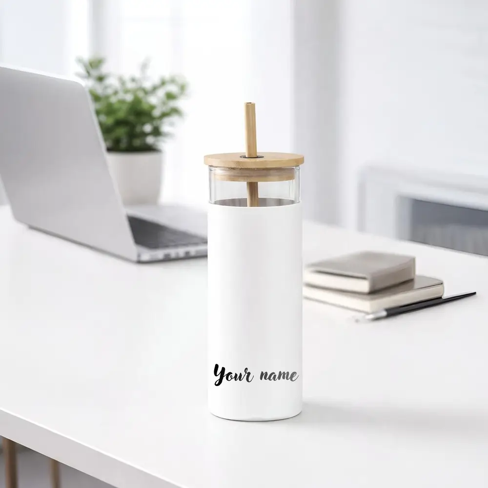 A white glass tumbler with a bamboo lid and straw on a desk, featuring "Your name" text in black script